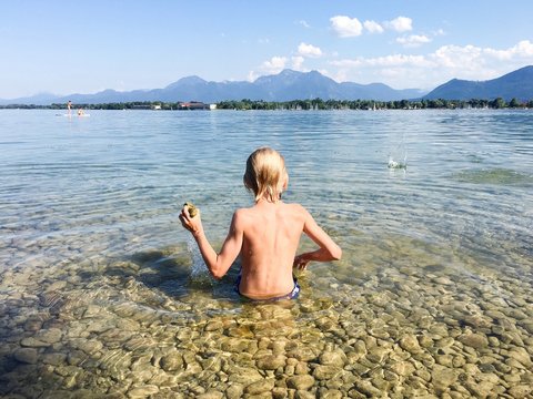 Rear View Of Shirtless Boy Sitting In Sea Against Sky
