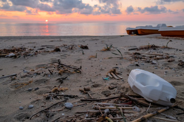 Plastic container waste on wild sea coast, sunset time,pollution cilento italy 