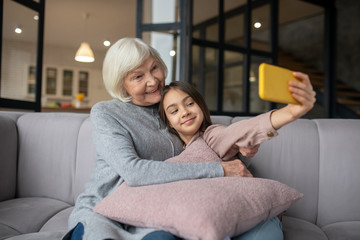 Obraz premium Granddaughter taking selfie with grandmother on the sofa at home.