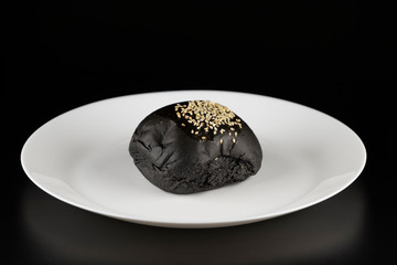 Loaf of charcoal bread bun with white sesame on top in the white plate isolated on black background