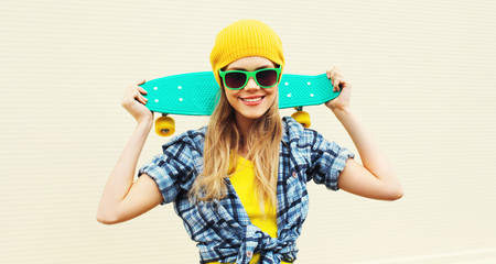 Portrait cool smiling woman with skateboard wearing colorful yellow hat on white background
