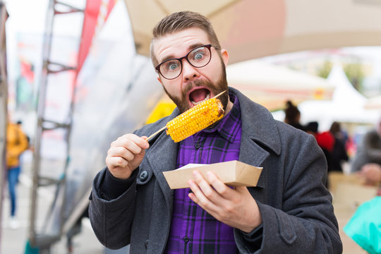 Handsome man eating roasted corn on the street.