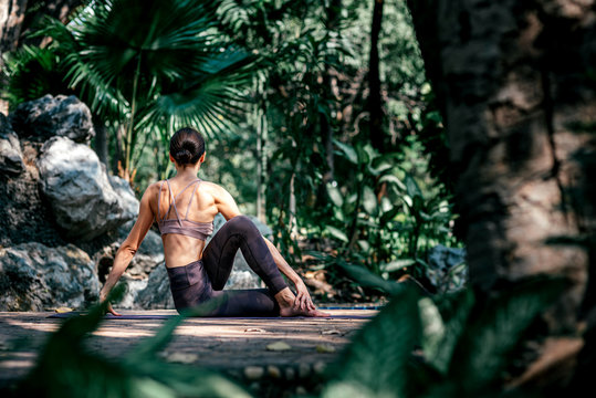 Relax your mind. Full-length shot of caucasian woman sitting in Seated Twist pose, Ardha Matsyendrasana while practicing yoga outdoors, in a garden. Healthy lifestyle and relaxation concept