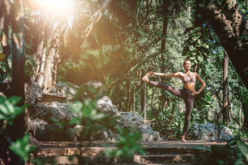 Full-length shot of caucasian woman standing in Extended Hand-to-Big-Toe pose, Utthita Hasta Padangusthasana while practicing yoga outdoors, in a garden. Healthy lifestyle and relaxation concept