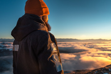 A man stands high in the mountains, at sunset, above the clouds.