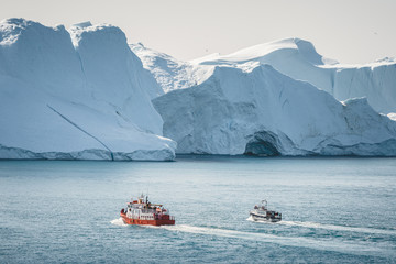 Orange whale Watching tour boat ship with icebergs in background. View towards Icefjord in Ilulissat. Greenland Disko Bay. Icebergs reflecting sunlight on a summer day.