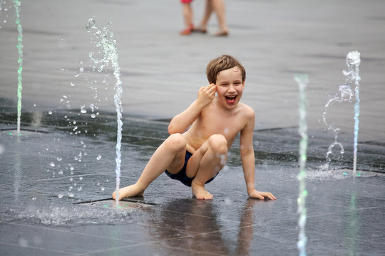 Cute Shirtless Boy Playing With Fountain On City Street