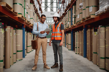 Young banker in conversation with warehouse manager holding digital tablet discussing loan details...