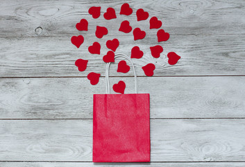 Red shopping bag and hearts on white wooden background. Valentines day concept. Top view, copy space, paper wrap, sale