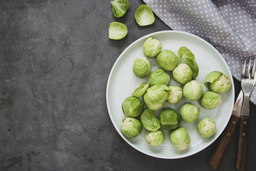 Fresh brussels sprouts in white plate isolated on dark background. Healthy vegan food, diet concept.