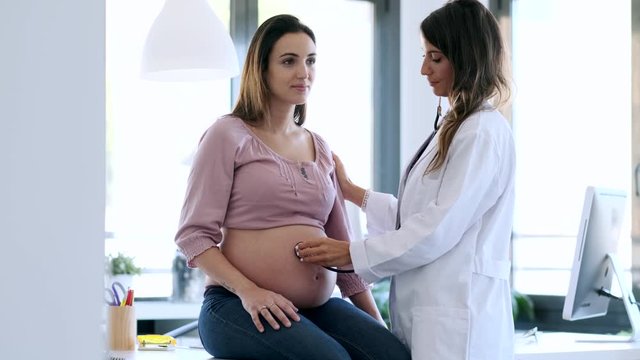 Pretty young woman gynecologist checking the heartbeat baby of her pregnant patient in the clinic.