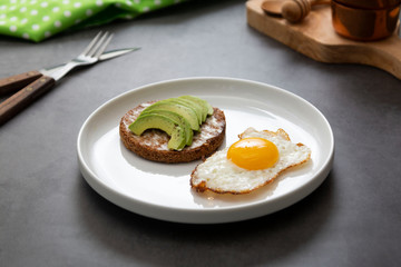 Avocado toasted sandwich and a fried egg on a white plate with asparagus. Healthy food or breakfast. Dark background.
