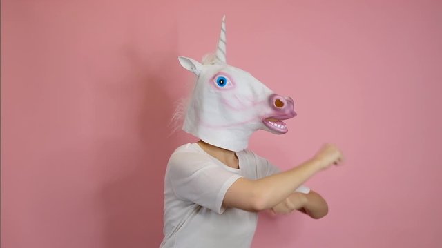 Weird funny video - woman with unicorn head dancing over pink background