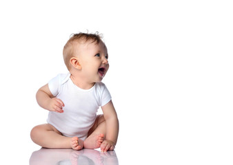 Happy laughing infant child baby boy toddler in white bodysuit is sitting on the floor looking at...