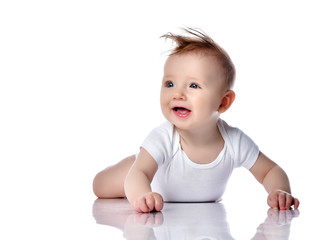 Happy smiling infant child baby boy toddler with blue eyes in white bodysuit lies on the floor on his stomach looking