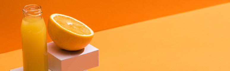 fresh juice in glass bottle near orange half and white cubes on orange background, panoramic shot