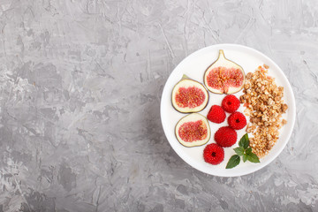 Yoghurt with raspberry, granola and figs in white plate on a gray concrete background and linen textile. top view