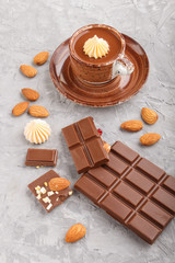 Cup of hot chocolate and pieces of milk chocolate with almonds on a gray concrete background. Side view.