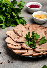 Boiled beef tongue with greens on a plate. Sauces and greens on the table.