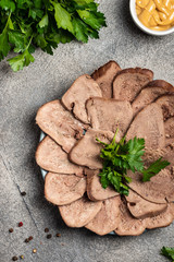 Boiled beef tongue with greens and mustard on a plate. Top view. Close-up.