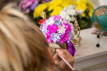 Naklejka premium A young blond woman is writing a note on a floral arrangement. The arrangement is made of white, purple and pink chrysanthemums placed in a wooden bark box.