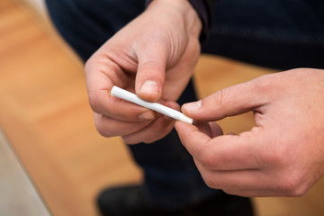 Closeup on the hands of a man holding a hand-wrapped cigarette. And he's getting ready to smoke it.