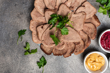 Boiled beef tongue with greens, mustard, horseradish sauce on a plate. Top view. Close-up.