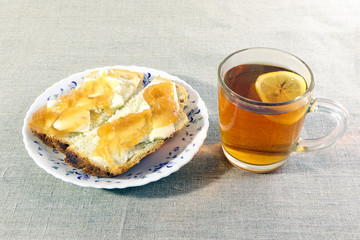 Two slices of white bread with butter and jam on a plate. Cup of tea with limon. Bright background.Breakfast.