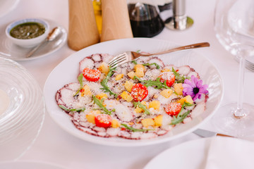 A stylish meat salad decorated with half tomatoes, pieces of cheese, greens and flower. Modern food in the restaurant.
