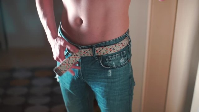 A man without a shirt unfastens his pants 