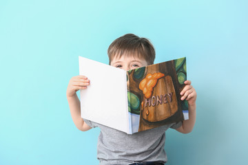 Cute little boy reading book on light background