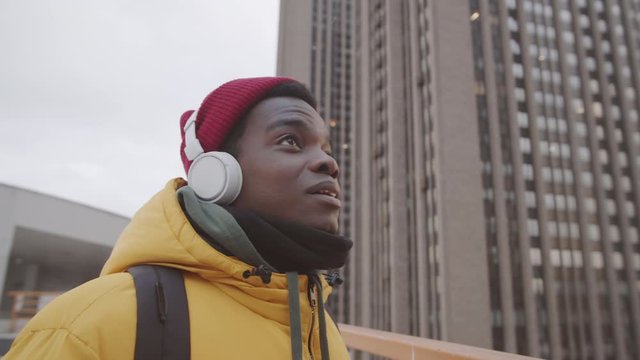 Close up of African hipster man standing outdoors with headphones on his head and enjoying audio book