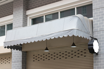 grey canvas awning over the white shutter door of shop with blank mock up. - obrazy, fototapety, plakaty