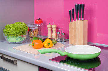 Green frying pan on modern black induction stove, cooker, hob or on cooktop in kitchen interior. Fresh vegetables lie near a frying pan on a gray table