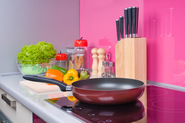Frying pan on modern black induction stove, on cooktop in kitchen interior. Fresh vegetables lie ...