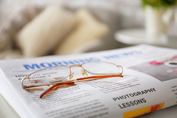 Stylish eyeglasses with newspaper on table at home, closeup