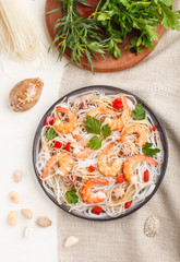 Rice noodles with shrimps or prawns and small octopuses on gray ceramic plate on a white wooden background. Top view, close up.