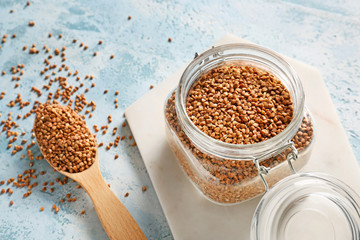 Jar and spoon with raw buckwheat on table