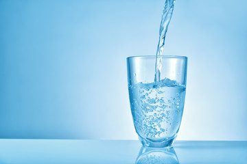Pouring of fresh water into glass on color background