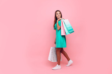 Portrait of a stylish smiling beautiful woman in an off-the-shoulder dress holding bags on an isolated pink background