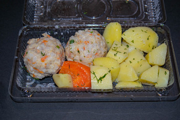 meat meatballs with boiled potatoes and boiled carrots in a plastic container on a dark background. Close up.