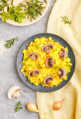Yellow fried rice with champignons mushrooms, turmeric and oregano on blue ceramic plate on a gray concrete background. top view.