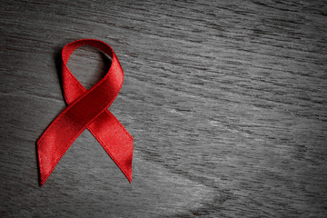 Red ribbon Aids awareness for World HIV/AIDS day on black and white wooden background. - obrazy, fototapety, plakaty