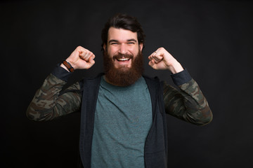 Long bearded man is smiling and making the winner gesture on black background.