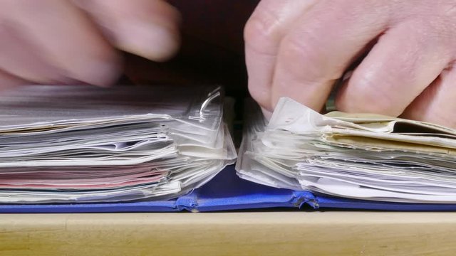 Close POV shot of a man&rsquo;s hands opening a ring binder full of business paperwork / documents in plastic pouches, then slotting in a new piece and closing the rings and the binder.