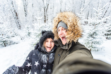 Fototapeta na wymiar Technologies and relationship concept - Happy smiling couple taking a selfie in a winter forest outside