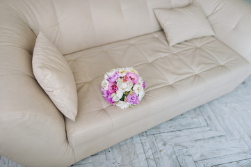 Flowers for the bride. Beautiful and stylish wedding bouquet with with pink and white peonies lies on the background of a beige, gray sofa. Wedding details and decorations.