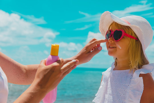 sun protection - mom put suncream on little girl face at beach