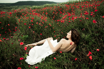 Woman is lying naked covered a white shirt among poppy flowers