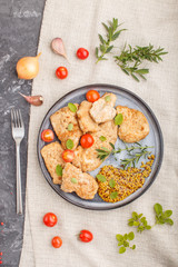 Fried pork chops with tomatoes and herbs on a gray ceramic plate on a black concrete background.  top view, close up.